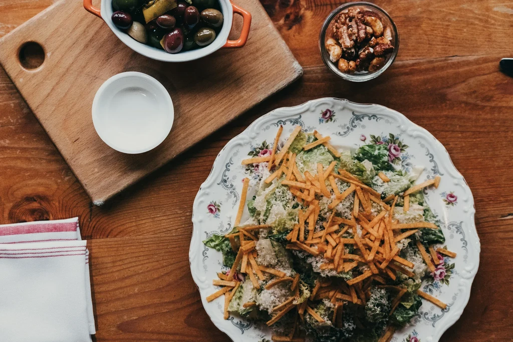 Overhead: wooden table with a salad plate, olives, nuts, and napkins.
