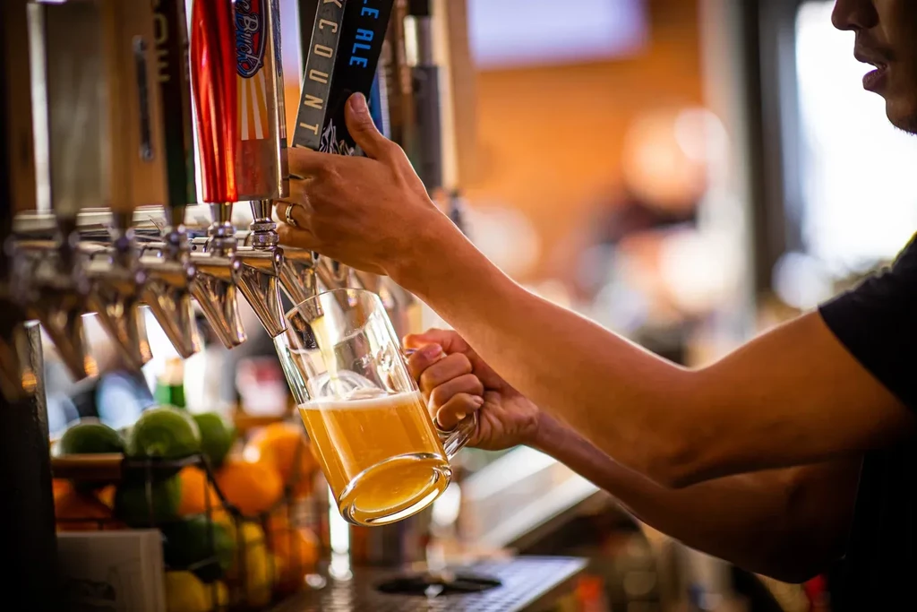 Bartender's hands pour golden beer from tap into glass mug.