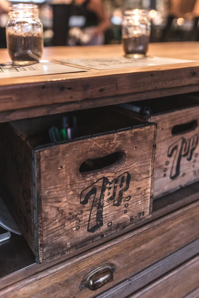 Vintage '7UP' crates below a rustic wooden counter with jars.