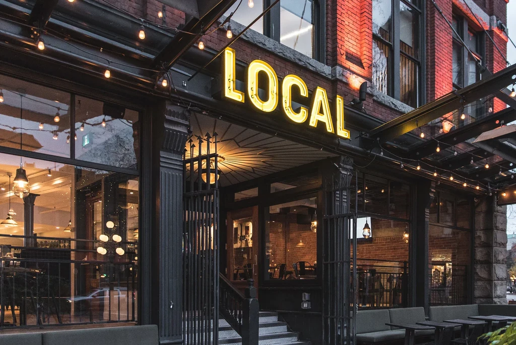 'LOCAL' restaurant exterior at dusk with bright neon sign and patio.