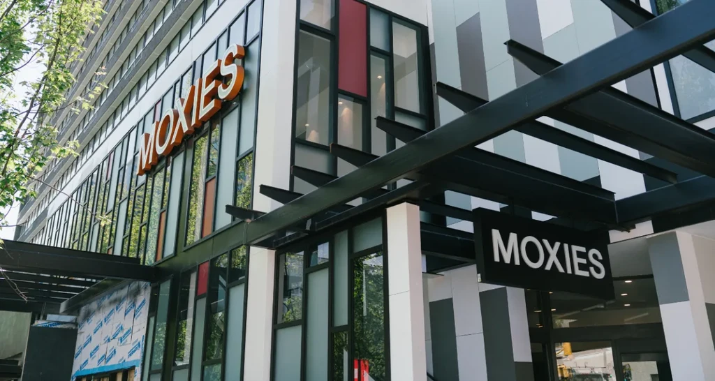 Modern building facade with large windows and two "Moxies" signs.