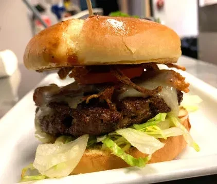 Tall gourmet beef hamburger with melted cheese, lettuce, tomato, fried onions.