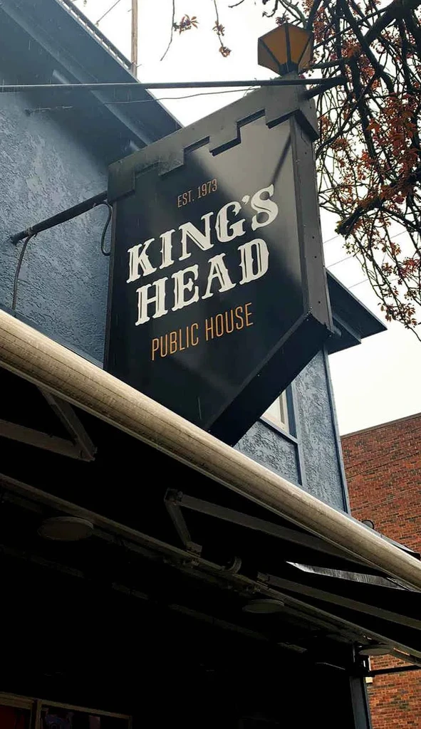 Black castle-turret 'KING'S HEAD' public house sign on building.