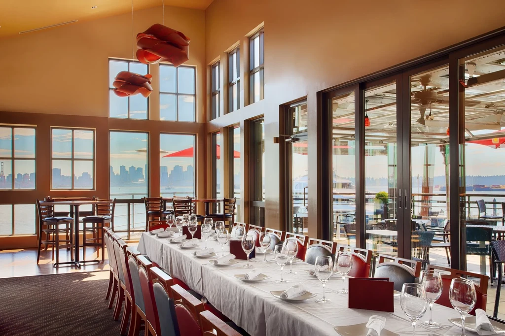 Empty elegant restaurant with set table and panoramic waterfront city view.