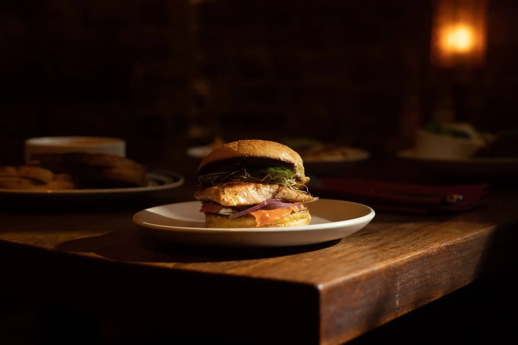 Gourmet grilled salmon and smoked fish burger on a wooden table.