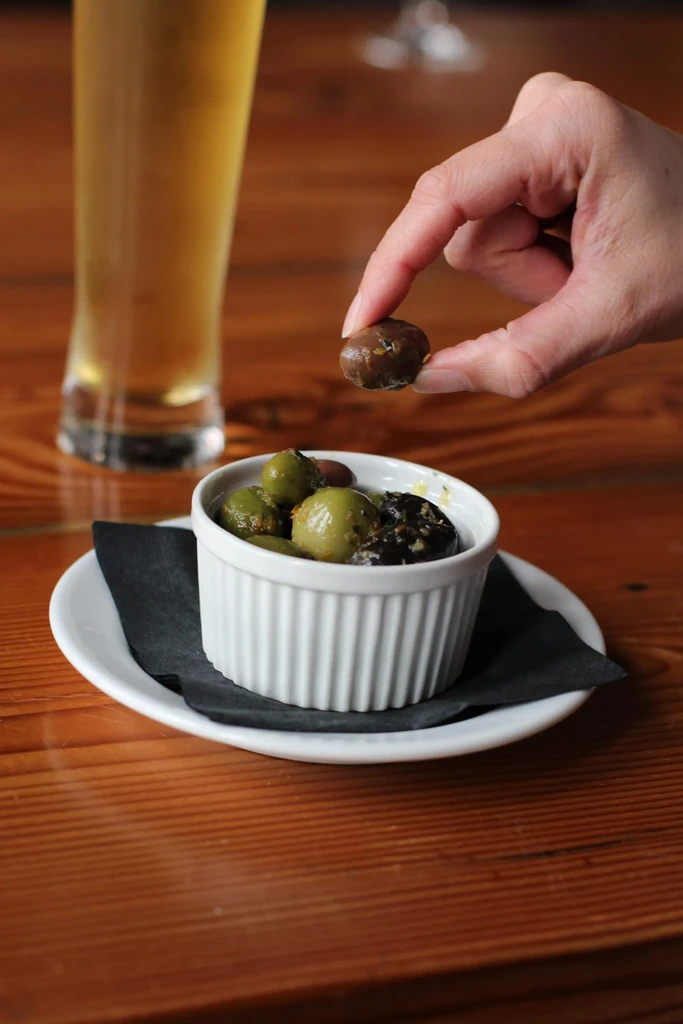Hand picking a dark olive from mixed olives next to a beer.