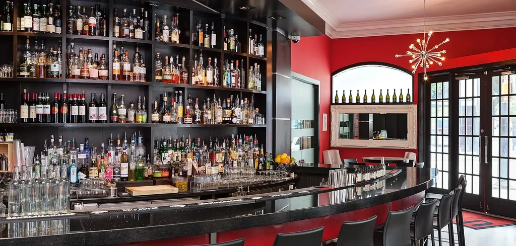 Modern bar with dark curved counter, liquor bottles, and red walls.