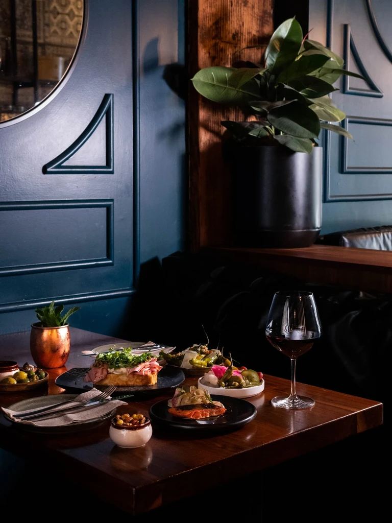 Open-faced sandwich, salmon, red wine, cutlery on dark restaurant table.
