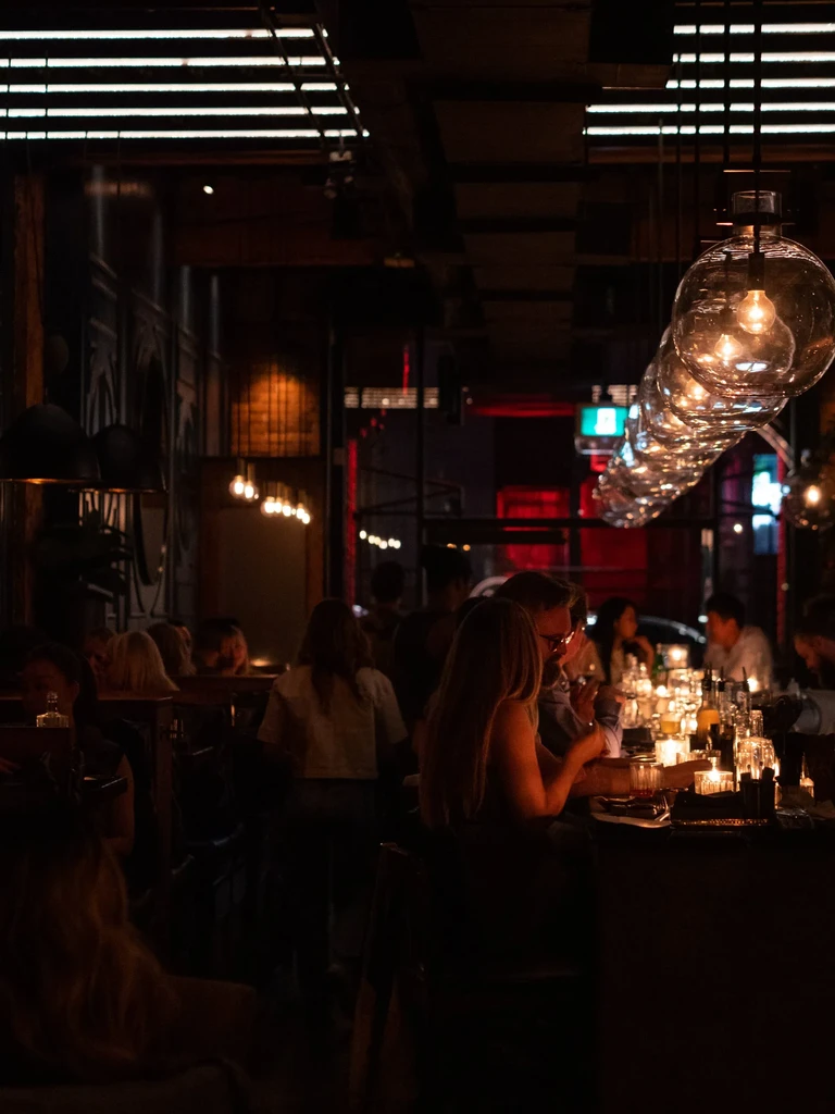 Dimly lit bar, warm globe lights, people at tables and counter.