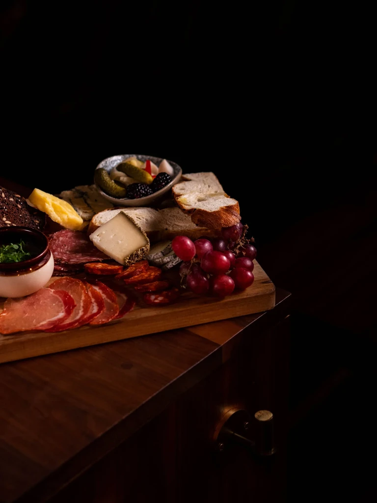 Dark charcuterie board with meats, cheeses, breads, grapes, and berries.