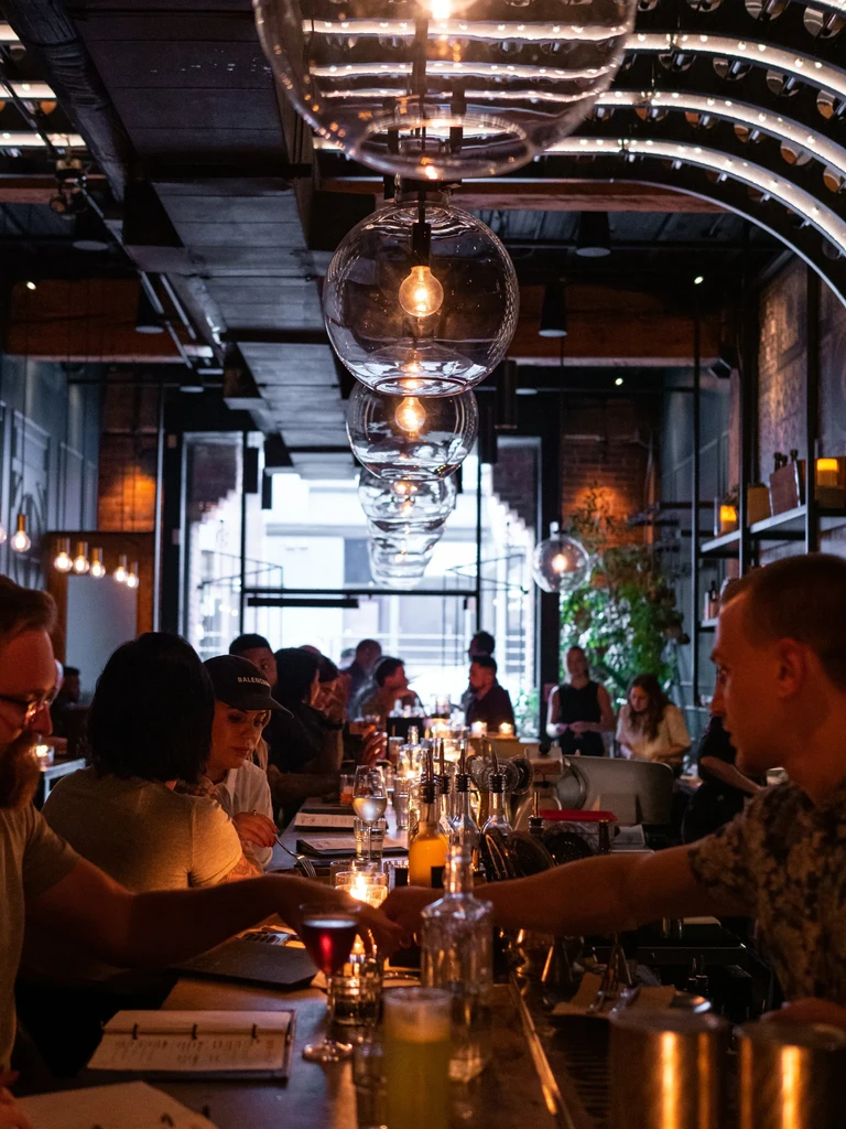 Warmly lit modern bar with patrons, bartender, and globe light fixtures.