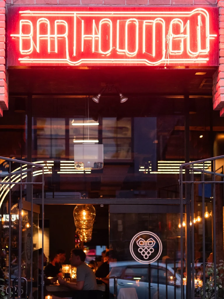 Entrance to BARTHOLOMEW: red neon sign, glass doors, lively interior.