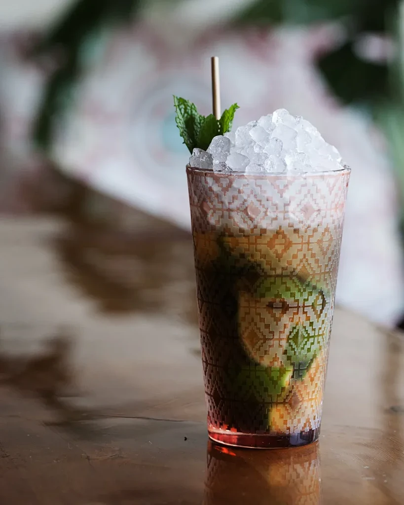 Cocktail with mint, lime, and ice in a tall, patterned geometric glass.