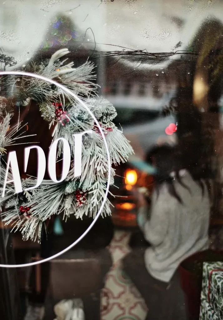 Frosted Christmas wreath and partial letters on window, blurry restaurant inside.