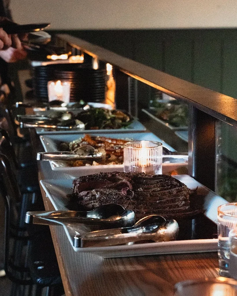 Rustic buffet table with sliced meat, vegetables, and warm candle light.