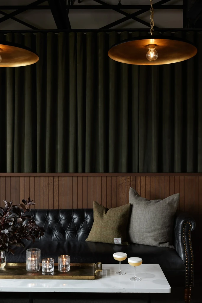 Dimly lit lounge with black sofa, marble table, cocktails, and gold lights.