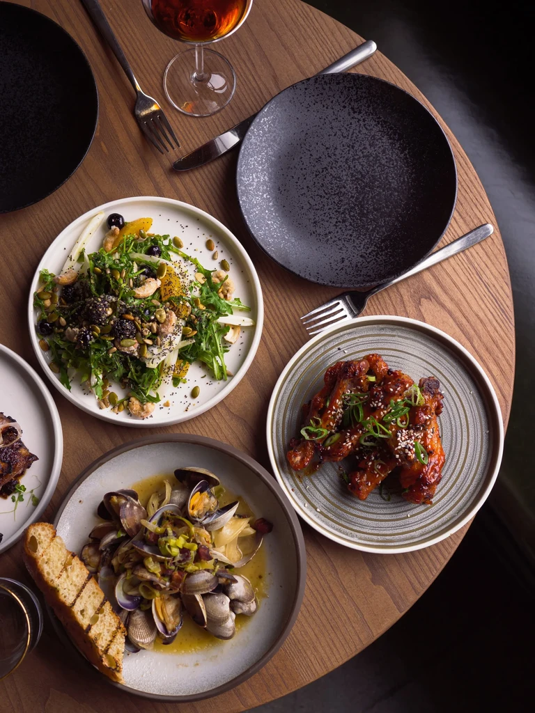 Overhead view: restaurant table with green salad, clams, glazed chicken wings.