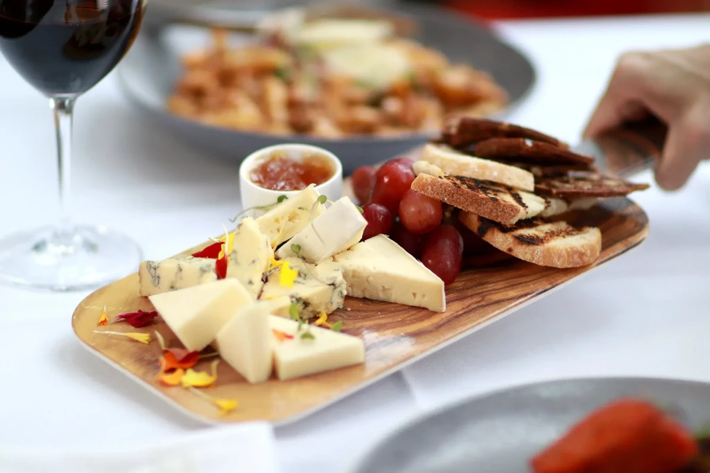 Cheese board with grapes, crackers, jam, and red wine.