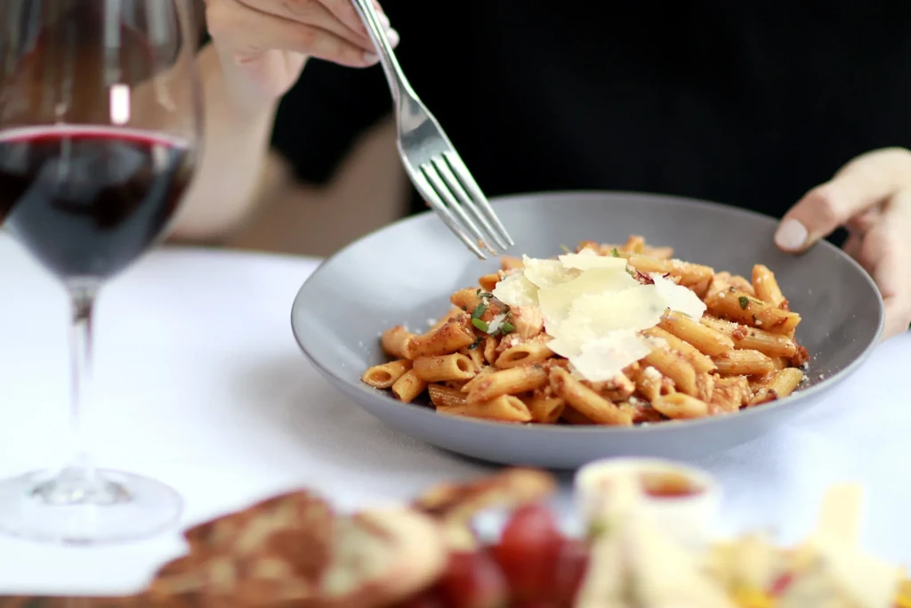 Hands with a fork poised over penne pasta with red sauce and Parmesan.