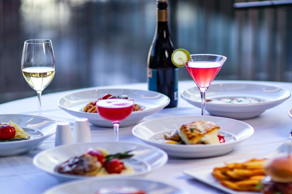 Plated gourmet dishes, wine, and colorful cocktails on a restaurant table.