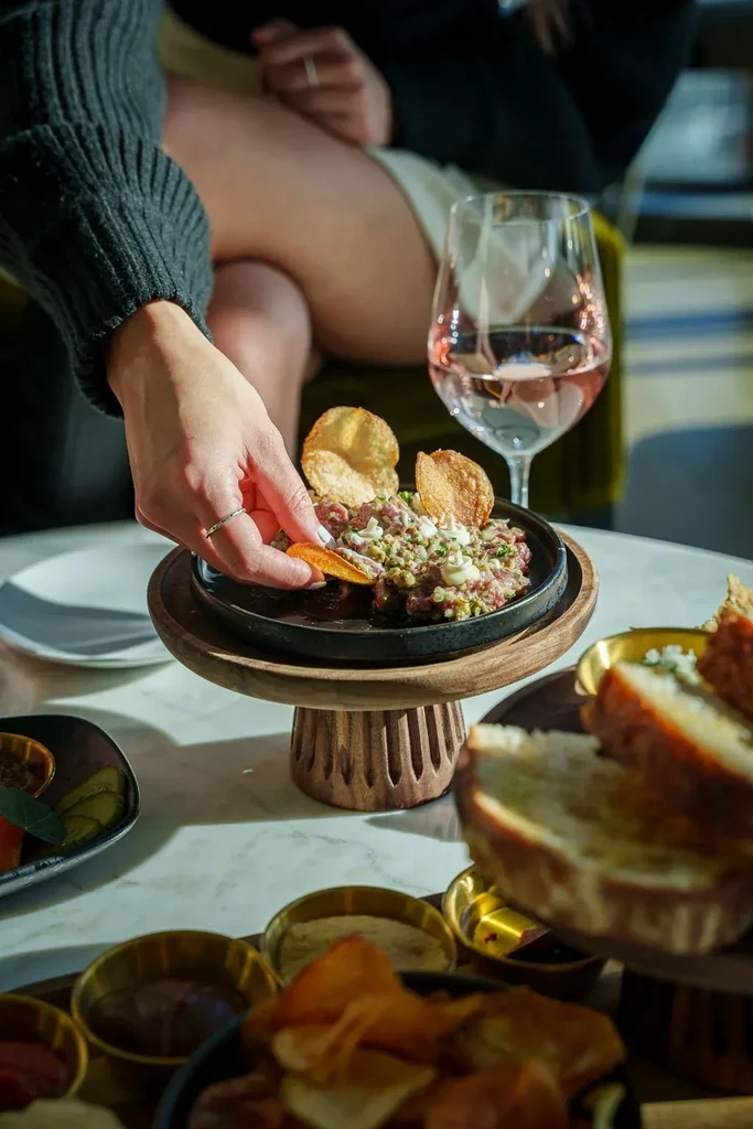 Close-up of tartare with chips, rosé, and a hand reaching.