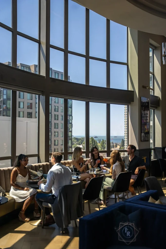 Six people socialize in an elegant restaurant with city and water views.