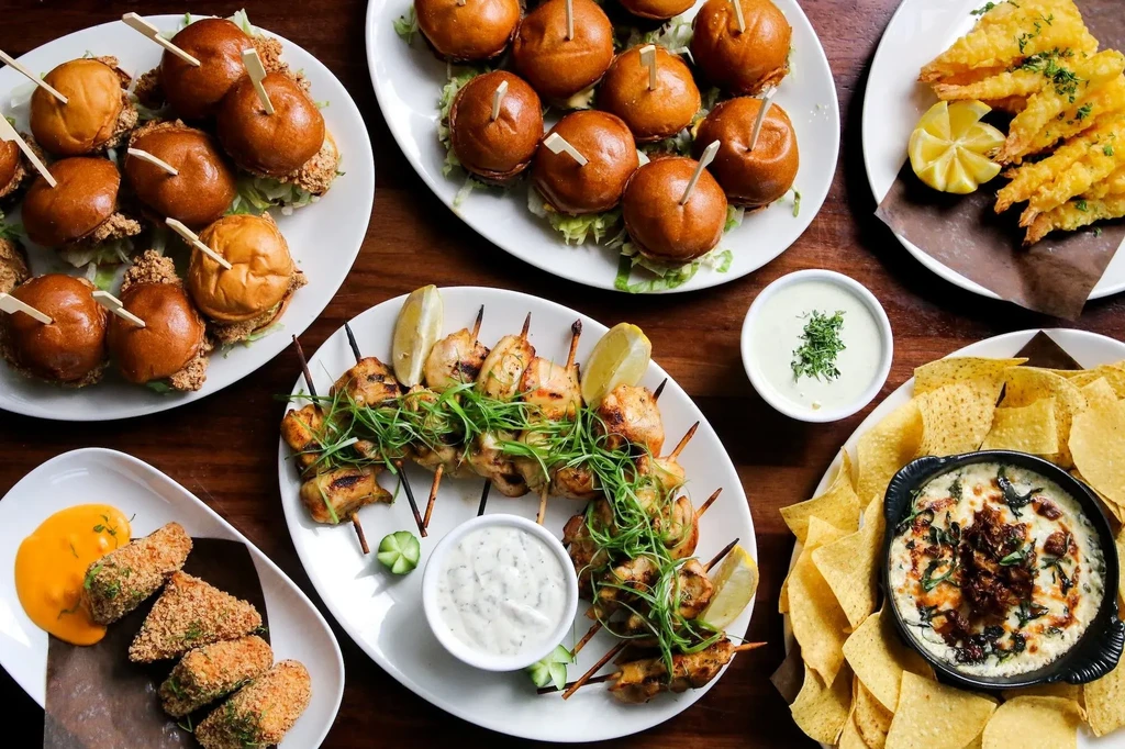 Top-down view of appetizer plates: sliders, shrimp, skewers, and dips.