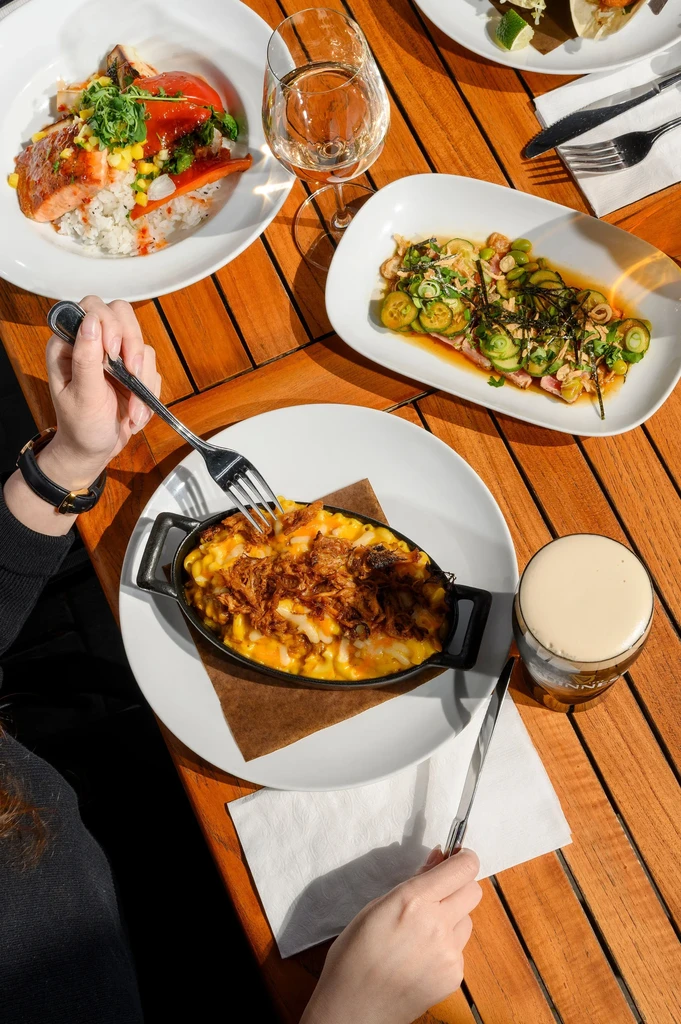 Overhead table view: salmon, mac and cheese, drinks, hands with utensils.