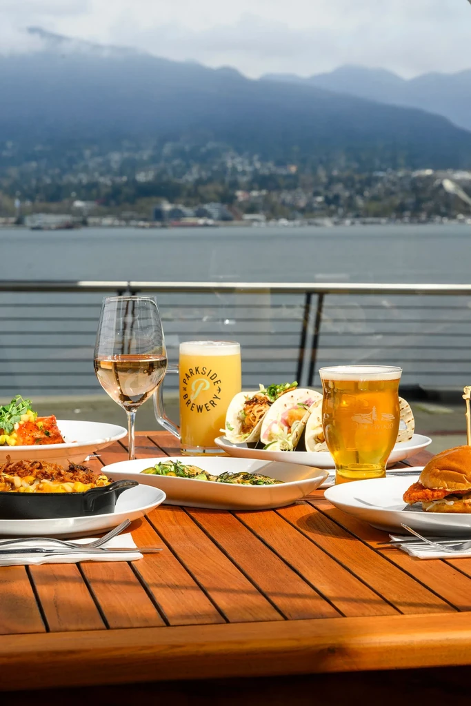 Outdoor table with varied food, drinks, and a scenic mountain cityscape.