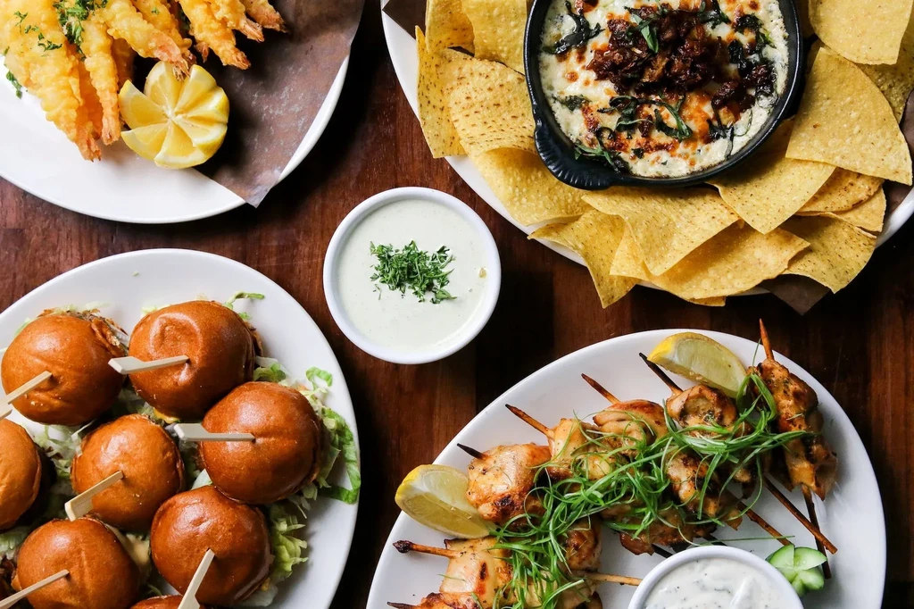 Overhead shot of fried shrimp, sliders, cheesy dip, and chicken skewers.