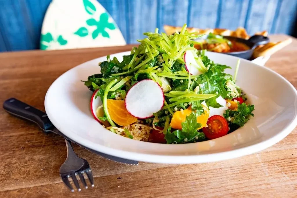 Colorful salad with greens, radish, orange, and quinoa on a table.