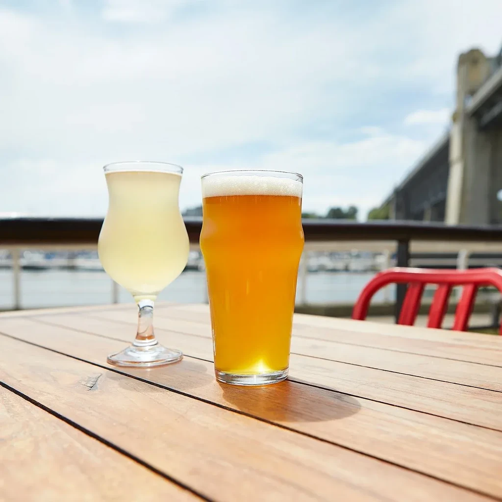 Two glasses of drinks on a wooden outdoor table by water.