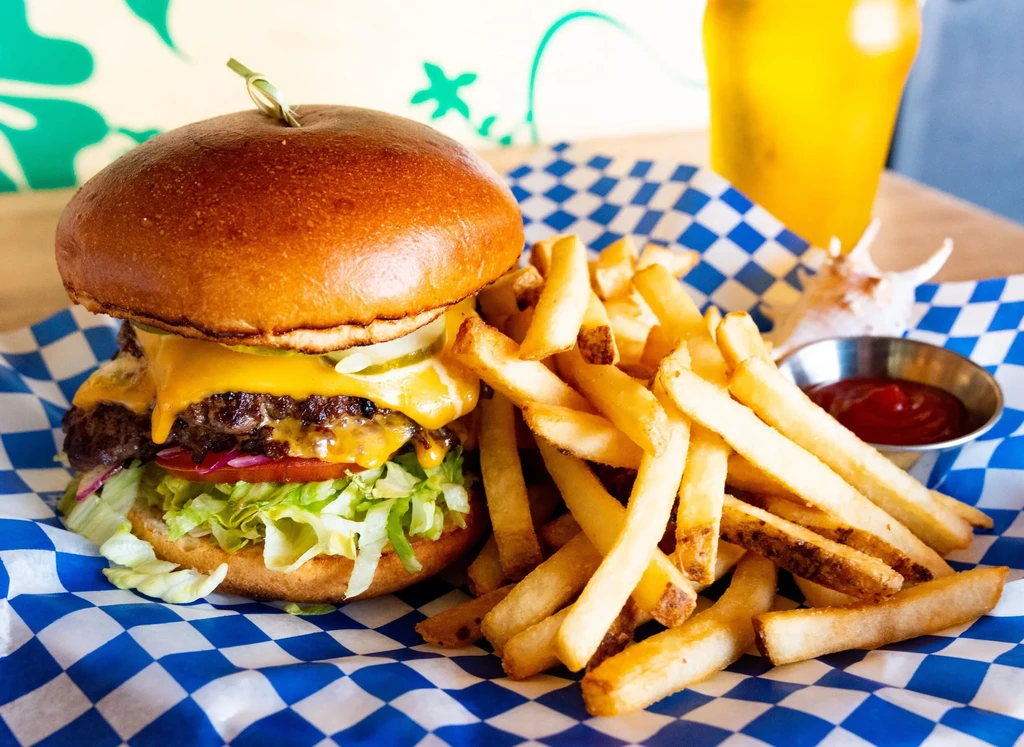 Tall cheeseburger, fries, and ketchup on checkered paper.