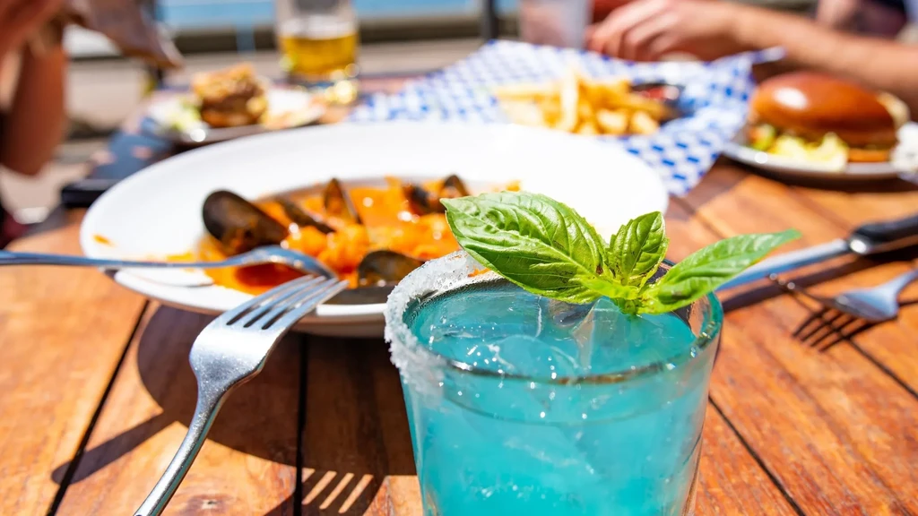 Blue cocktail, mussels, burger, and fries on a rustic outdoor table.