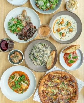 Flat lay of diverse restaurant dishes and drinks on a wooden table.