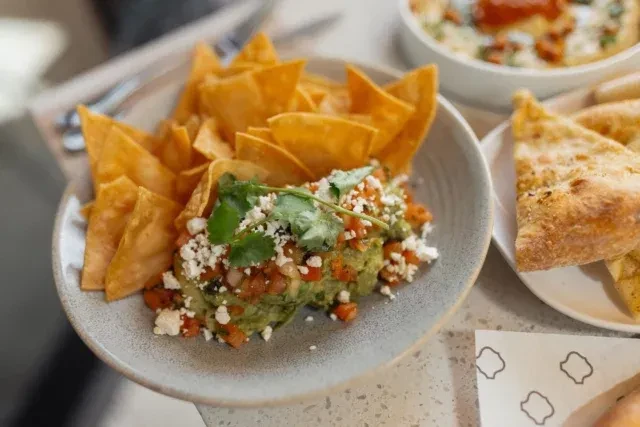 Vibrant green guacamole with diced tomatoes, cheese, cilantro, and tortilla chips.