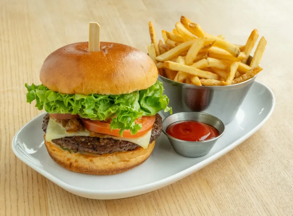 Stacked burger with cheese, lettuce, tomatoes, fries, and ketchup.