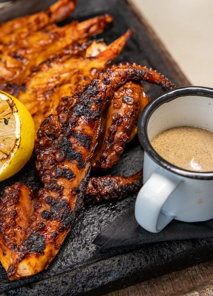 Charred octopus tentacle with grilled lemon, sauce, and other seafood.