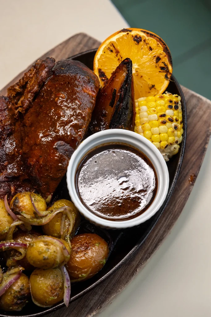 Barbecue dish with meat, potatoes, corn, and orange on skillet.