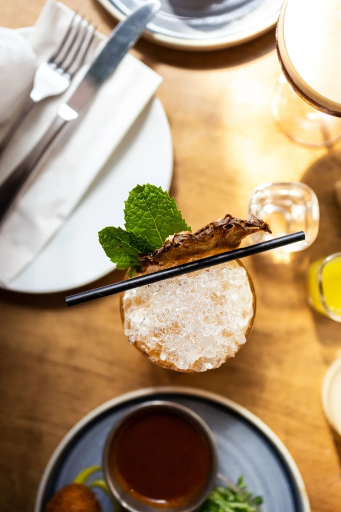 Amber cocktail with crushed ice, mint, and dried fruit on a table.