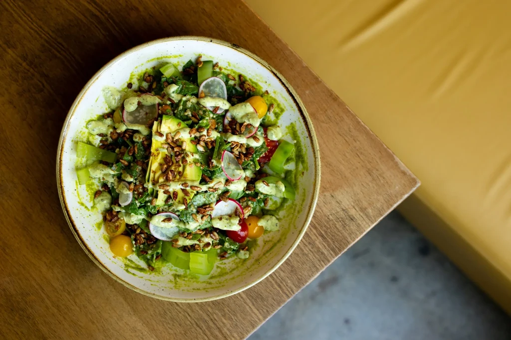 Vibrant salad with greens, avocado, tomatoes, radishes, dressing, and seeds.