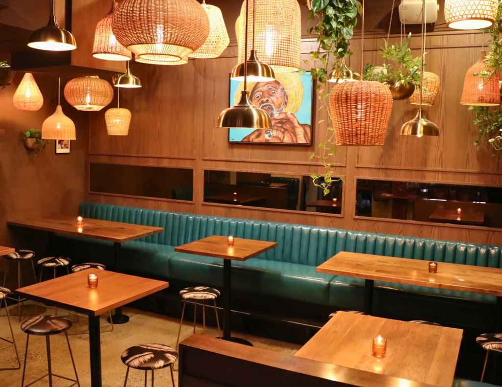 Warm restaurant interior with teal banquette, rattan lights, and lush plants.
