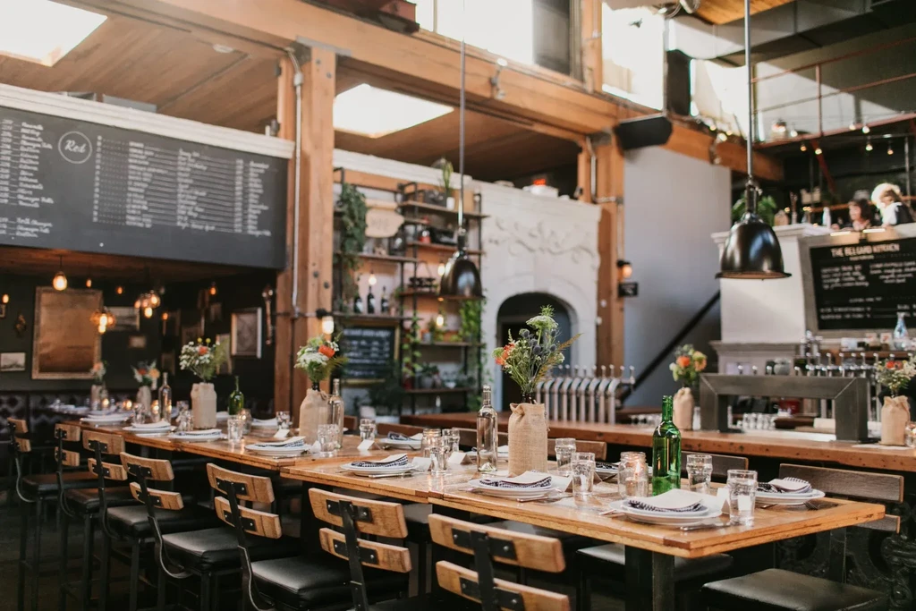 Warm, industrial-style restaurant interior with communal tables and a bar.