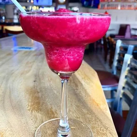 Fuchsia frozen drink in a margarita glass on a wooden table.
