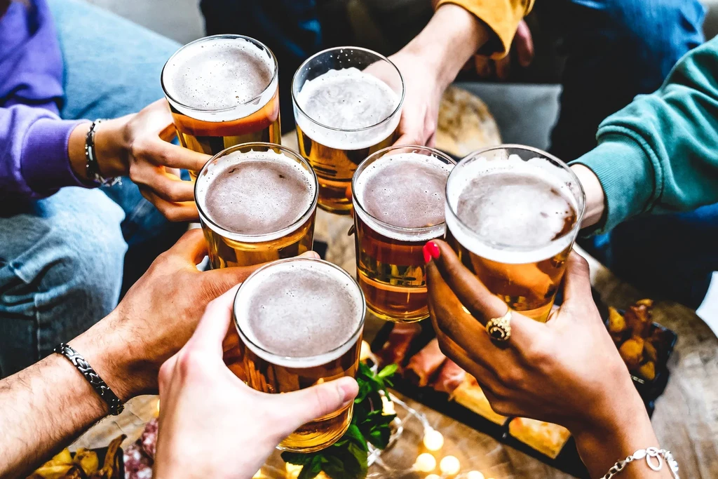 Diverse hands raise beer glasses, toasting at a lively gathering.