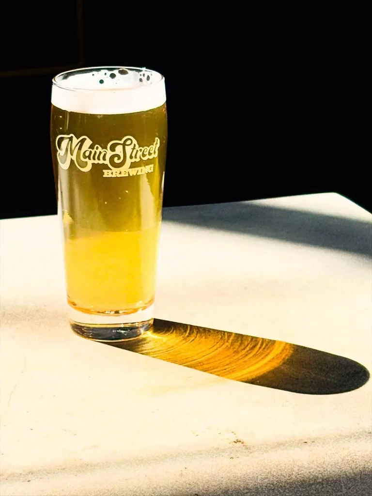 Main Street Brewing beer in a glass, sunlit with foam and shadow.