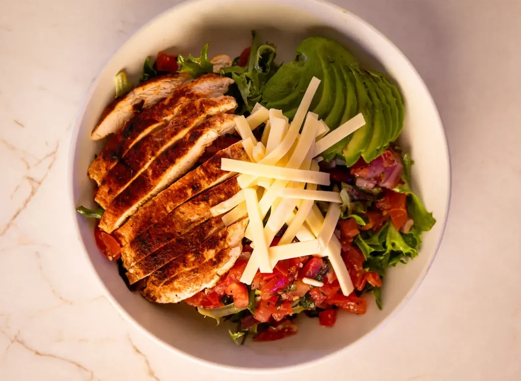Grilled chicken salad with avocado, shredded cheese, lettuce, and tomato.
