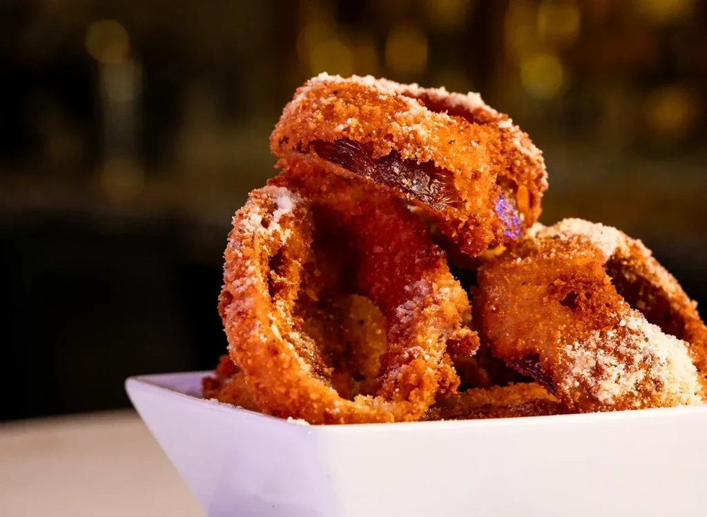 Golden-brown, heavily breaded onion rings piled in a white bowl.