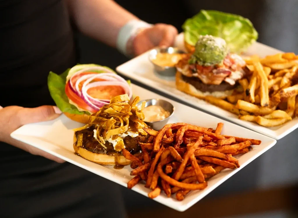 Two burger meals with fries, held by restaurant staff.