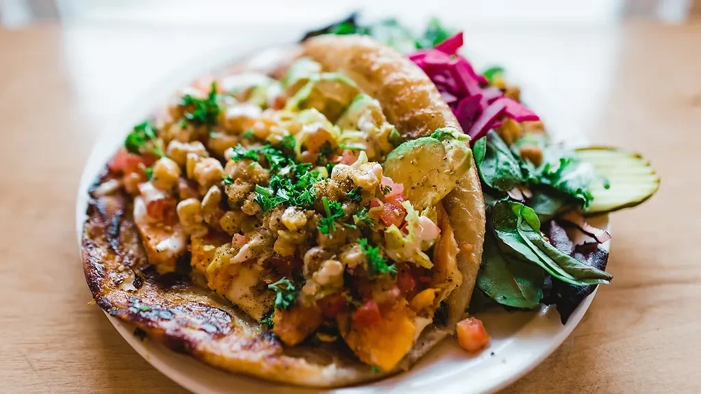Open-faced flatbread with chicken, chickpeas, avocado, herbs, tomatoes, and green salad.